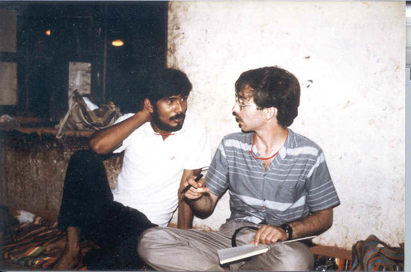 Two men seated cross legged on the floor in conversation