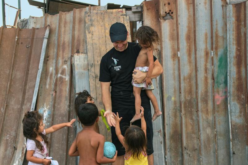 Gabriel carrying one child and playing with four others by broken down fence