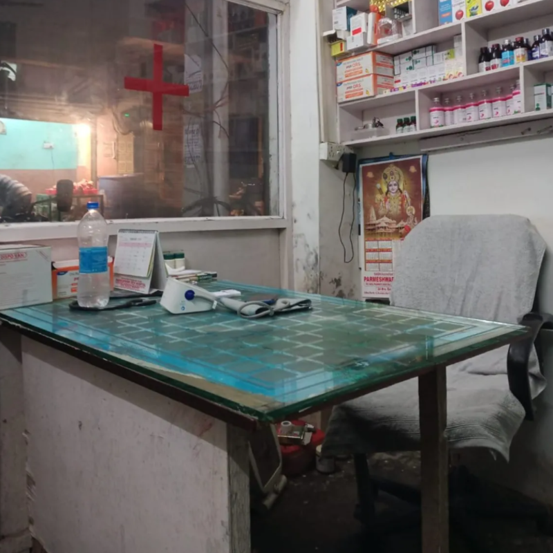 a makeshift office with a red cross on the window and medicines displayed behind the desk.