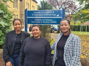 Three women standing in a line outside the department buildings, under a sign for the Institute for Science, Innovation and Society (InSIS)