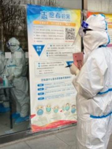 A staff member dressed in hazmat suit, standing in front of a poster with an illustration of people dressed similarly. (Photo by author.)